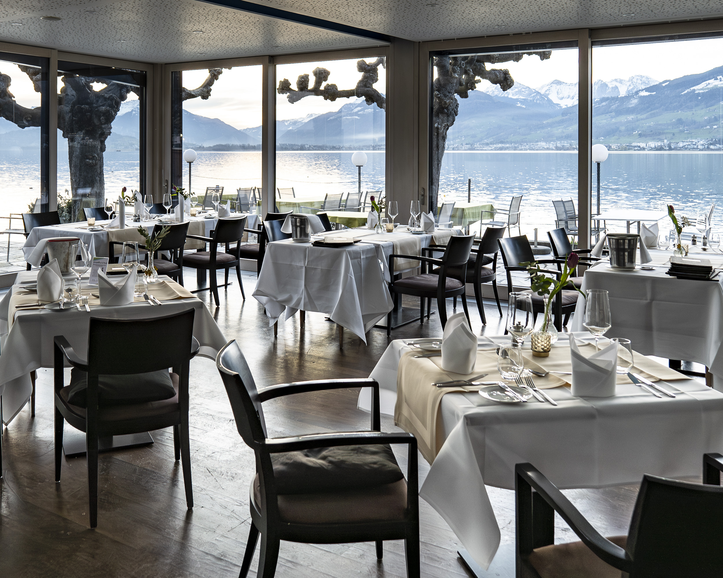 Im Seepavillon im Rössli Hurden sind die Restauranttische gedeckt. Die Fensterfront gibt den Blick frei auf den See und die Berge.