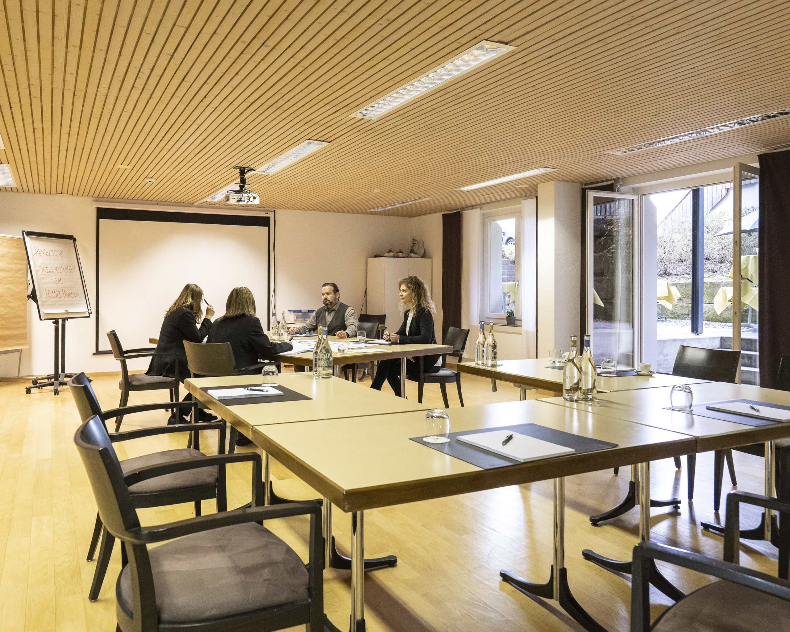 Der grosse Seminarraum im Rössli Hurden. Vier Personen sitzen an einem Tisch. Der Raum hat grosse Fenster und eine Glastür zur Terrasse.